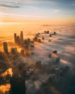 A high angle shot of a cityscape with tall skyscrapers during sunset covered with white clouds