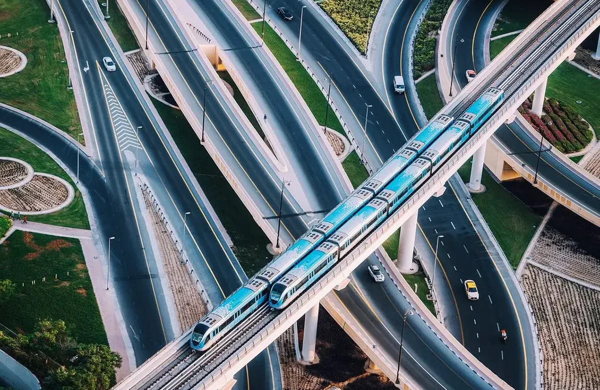 Dubai Metro Blue Line Impact: Aerial top-down view of the Dubai Metro track crossing complex highway interchanges, highlighting prime urban connectivity for real estate investments.