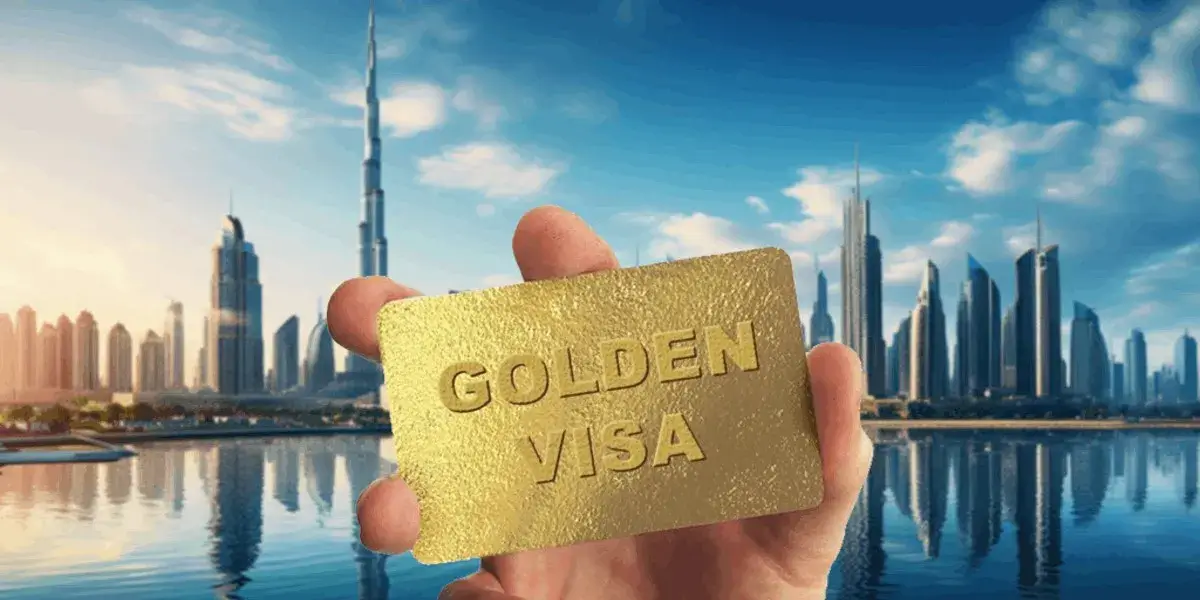 Dubai Golden Visa Real Estate 2026: A hand proudly holding a physical UAE Golden Visa card against the backdrop of the modern Dubai skyline and clear blue waters.